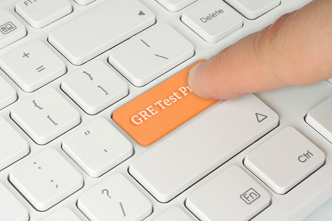 Person's finger pressing a GRE Test Program button on a computer keyboard