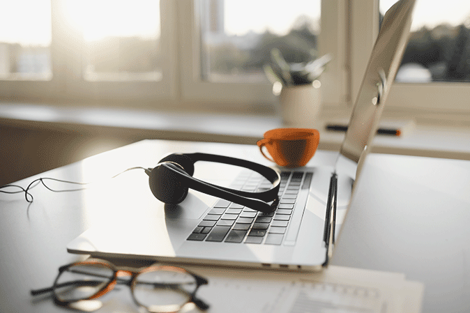 Laptop with headphones, coffee, and glasses on a desk representing a remote work setup